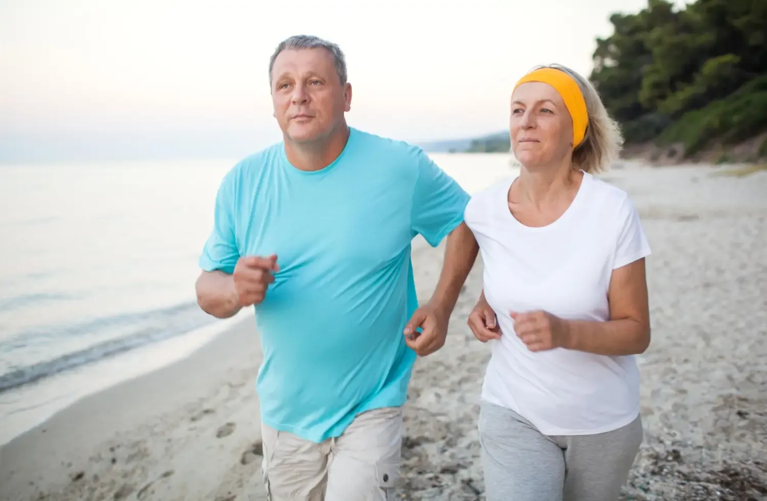 Active middle-aged couple jogging together on a beach, showing long-term lifestyle changes during Mounjaro® treatment